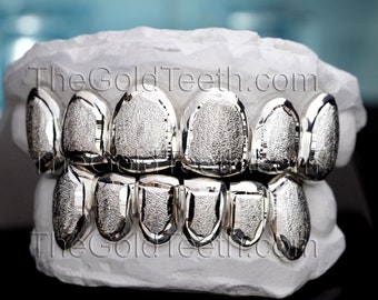 May include: A set of silver grillz with a textured finish. The grillz are displayed on a white mold of a mouth. The text "TheGoldTeeth.com" is visible on the mold.