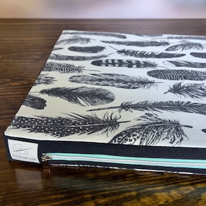 May include: A black and white feather print zippered cushion with a teal zipper and the text "One Brown Paw" on the bottom.