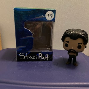May include: A custom-painted Funko Pop figure box with a blue, green and white paint design. The box has a clear plastic window and the text "Staci Pratt" is written on the front. The number "15" is written in a circle on the top of the box.