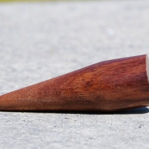 May include: A wooden, cone-shaped tool with a rounded tip. The tool is made of dark reddish-brown wood and has a smooth, polished finish.