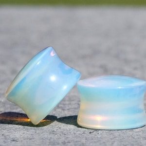 May include: Pair of iridescent blue and white opal ear gauges. The gauges are slightly flared and have a smooth, polished finish.