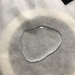 Puede incluir: Primer plano de una toalla de papel blanca texturizada con una sola gota de agua sobre ella.