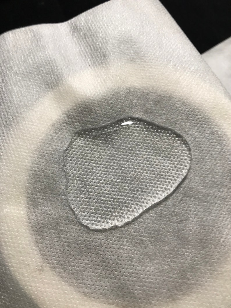 Puede incluir: Primer plano de una toalla de papel blanca texturizada con una sola gota de agua sobre ella.