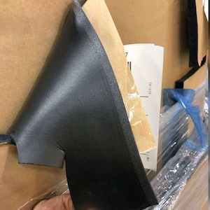 Puede incluir: Primer plano de una lámina de espuma negra con respaldo de papel marrón. La lámina de espuma está siendo sostenida por una mano y está parcialmente despegada para revelar el papel marrón.