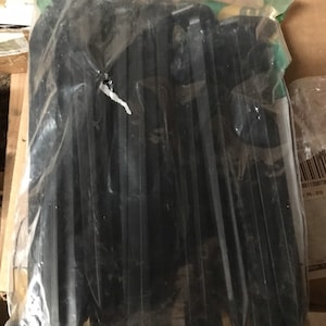 Puede incluir: Un paquete de estacas de tienda de campaña de plástico negro. Las estacas están agrupadas y envueltas en plástico transparente.