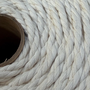 May include: Close-up of a tightly coiled, off-white rope. The rope is thick and appears to be made of twisted fibers. The texture is visible, with each strand clearly defined. A brown cardboard tube is visible in the center of the coil.