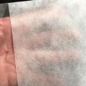 Puede incluir: Primer plano de una tela no tejida blanca con una superficie texturizada. La tela es suave y ligera.