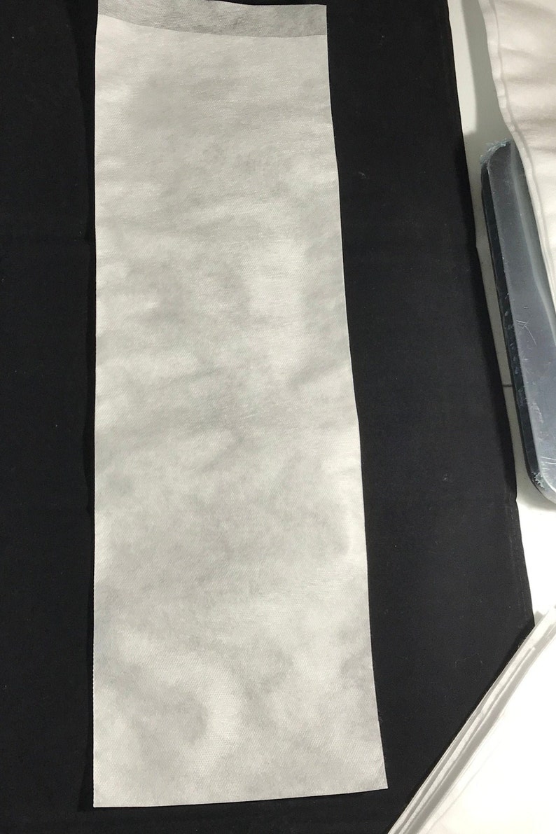 Puede incluir: Una hoja rectangular blanca de tejido no tejido, a menudo utilizada para presionar o planchar telas delicadas.