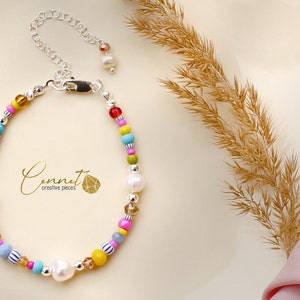 Könnte beinhalten: Ein farbenfrohes Perlenarmband mit weißen Perlen, silbernen Akzenten und einem Karabinerverschluss. Das Armband ist in verschiedenen Farben gehalten, darunter Rot, Blau, Gelb, Grün und Pink. Der Text "Connect creative pieces" ist auf dem Armband sichtbar.