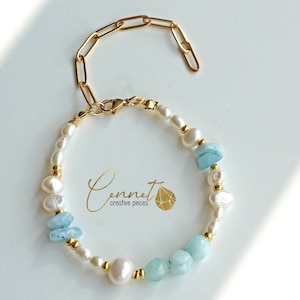 Könnte beinhalten: Ein Armband mit Süßwasserperlen, hellblauen Aquamarinsteinen und goldfarbenen Akzenten. Das Armband hat eine goldfarbene Kette und einen Verschluss. Der Markenname "Connet creative pieces" ist sichtbar.