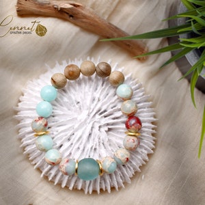 Könnte beinhalten: Ein Armband aus hellblauen, roten und braunen Perlen. Das Armband liegt auf einer weißen korallenartigen Oberfläche.