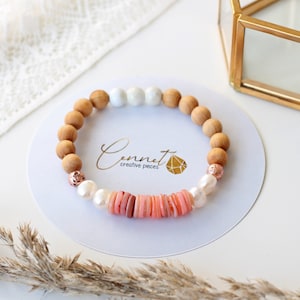 May include: A bracelet made with wooden beads, pink shell beads, white pearls, and rose gold accents. The bracelet is on a white background with the text "Cennet creative pieces".