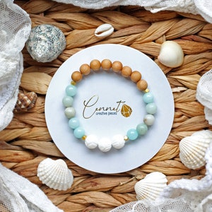 Könnte beinhalten: Ein hellblaues und braunes Perlenarmband mit weißen Muschelanhängern. Das Armband liegt auf einem weißen Hintergrund mit dem Text "Cennet creative pieces".