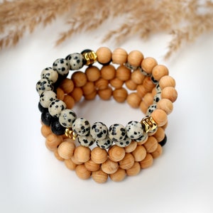 May include: A layered bracelet with wooden beads and black and white dalmatian jasper beads. The bracelet has gold spacers between the beads.