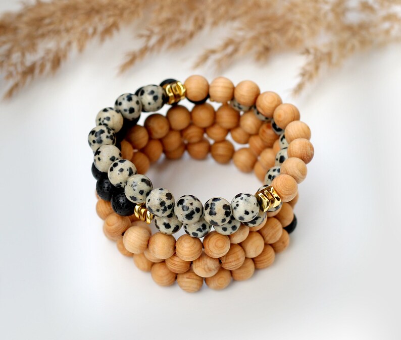May include: A layered bracelet with wooden beads and black and white dalmatian jasper beads. The bracelet has gold spacers between the beads.