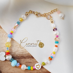 May include: A colourful beaded bracelet with a gold chain clasp and two white heart charms. The beads are a mix of white pearls, colourful glass beads, and small gold beads.