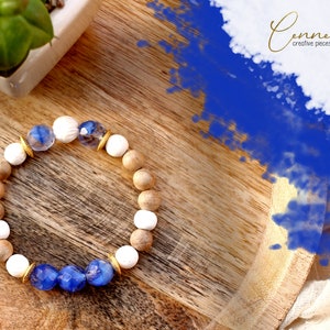 Könnte beinhalten: Ein Armband aus Holz und blauem Glas mit goldenen Akzenten. Das Armband liegt auf einer Holzoberfläche.