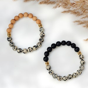 May include: Two bracelets made with natural stones. One bracelet is made with brown wood beads and white and black dalmatian jasper beads. The other bracelet is made with black lava beads and white and black dalmatian jasper beads. Both bracelets have gold spacers.