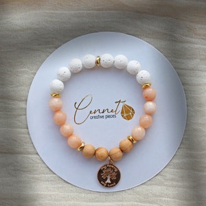 Könnte beinhalten: Ein Armband aus weißen und pfirsichfarbenen Perlen, Holzperlen und einem goldenen Anhänger mit den Worten "My Family My Love" und einem Baumdesign.