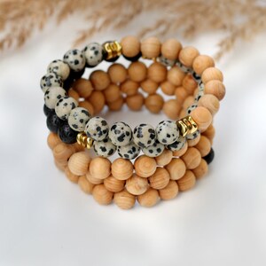 May include: A layered bracelet with black and white speckled beads, brown wooden beads, and gold spacers.
