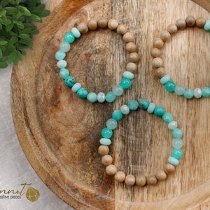 Könnte beinhalten: Drei Armbänder mit türkisfarbenen und hellblauen Perlen auf einer Holzoberfläche. Die Armbänder bestehen aus Holzperlen und türkisfarbenen und hellblauen Edelsteinperlen.