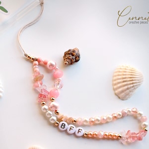 Puede incluir: Un brazalete de cuentas rosa y dorado con la palabra "BFF" escrita en letras blancas. El brazalete está hecho con cuentas rosas y blancas, cuentas doradas y pequeños cristales rosas y transparentes.