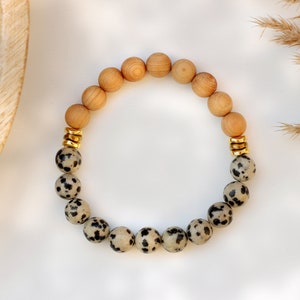 May include: A bracelet made with brown wooden beads and black and white dalmatian jasper beads. The bracelet has gold spacers between the beads.