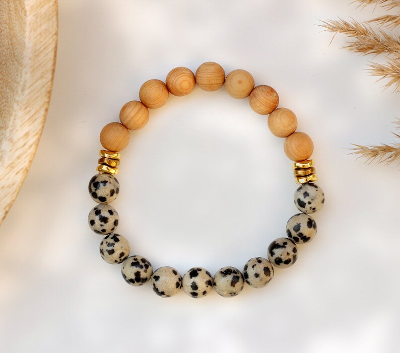 May include: A bracelet made with brown wooden beads and black and white dalmatian jasper beads. The bracelet has gold spacers between the beads.