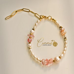 Op de afbeelding: Een delicate armband met een mix van witte en roze parels, afgewisseld met goudkleurige metalen accenten en roze edelstenen. De armband heeft een gouden ketting en sluiting. De merknaam "Cennet creative pieces" is zichtbaar.