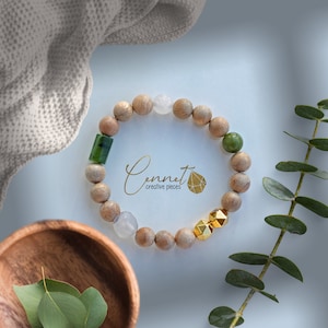 May include: A wooden beaded bracelet with green, white, and gold accents. The bracelet is made of natural wood beads and features a variety of stones, including jade, white agate, and gold-toned metal beads. The bracelet is a beautiful and unique piece of jewelry that would make a great gift for any occasion.