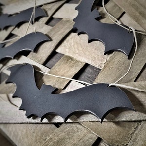 May include: A string of black bats hanging on a wooden surface. The bats are cut out of paper or cardboard and are strung together with twine.