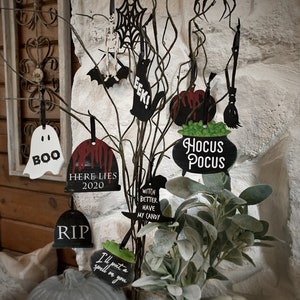 May include: A set of 10 Halloween-themed SVG cut files. The files include a ghost, a spider, a witch's hat, a cauldron, a broom, a tombstone, a bat, a spiderweb, a pumpkin, and a sign that says "Here Lies 2020".