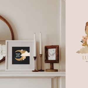 K&ouml;nnte beinhalten: Ein wei&szlig;er gerahmter Druck mit schwarzem Hintergrund und goldenem Halbmond mit dem Text "bloom with grace" und floralen Illustrationen. Der Druck befindet sich auf einem wei&szlig;en Kaminsims mit zwei Kerzenst&auml;ndern und einem kleinen Holzrahmen mit einer Schwarzwei&szlig;zeichnung.