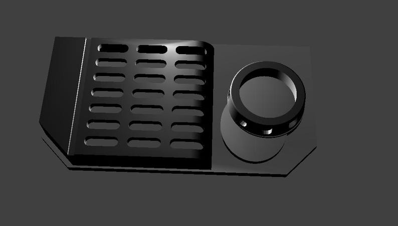 May include: Black plastic part with a rectangular grid pattern and a round hole with a smaller ring inside.