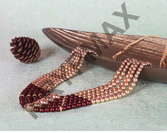 May include: A multi-strand necklace made of gold and burgundy beads. The necklace is displayed on a wooden tray.