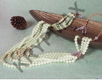 Pode incluir: Um colar de pérolas de várias camadas com um pingente de ouro e strass. O colar é feito de pérolas de cor creme e tem um design em camadas.