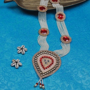 Op de afbeelding: Een witte parelketting met rode en gouden accenten. De ketting heeft een grote traanvormige hanger met rode en gouden versieringen.