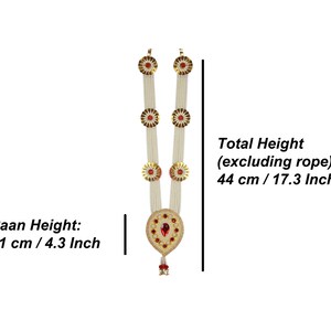 Op de afbeelding: Een witte parelkrans met gouden en rode accenten. De krans heeft drie ronde decoratieve elementen met rode edelstenen in het midden. De krans is 44 cm hoog en 11 cm breed.