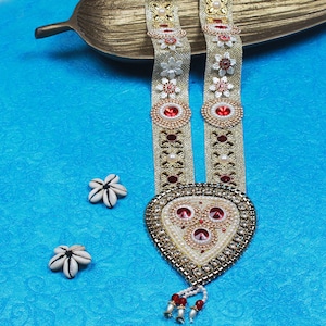 Op de afbeelding: Een gouden en witte kralenketting met rode en witte bloemen en een hartvormige hanger met rode strass steentjes. De ketting ligt op een blauwe achtergrond.