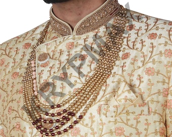May include: A cream-colored men's garment with a gold embroidered floral pattern and a gold beaded necklace. The garment has a high collar with a gold beaded trim.