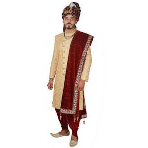 May include: A man wearing a gold embroidered sherwani with a maroon velvet shawl and a gold turban. The shawl has gold embroidery and tassels.