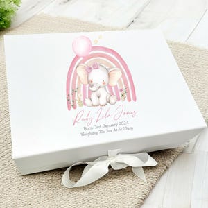 May include: A white keepsake box with a pink and orange rainbow and a pink elephant holding a balloon. The box is decorated with the text "Ruby Vila Jones", "Born: 3rd January 2024", and "Weighing 7lb 3oz At: 9:23am".