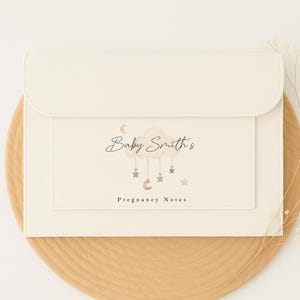 May include: A white envelope with a cream coloured flap. The envelope has a design of a cloud with stars and a crescent moon hanging from it. The text "Baby Smith's Pregnancy Notes" is printed on the envelope.