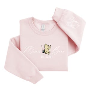 May include: Pink sweatshirt with a white graphic of Winnie the Pooh and Piglet with the text "Mama Bear Est. 2024". The right sleeve has the text "Jolie Olivia" with a heart.