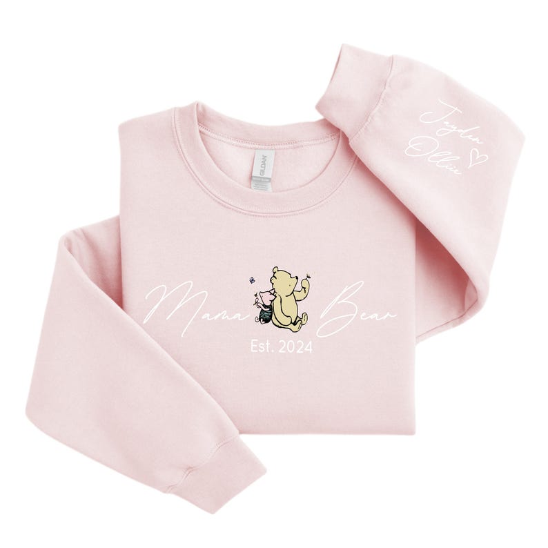 May include: Pink sweatshirt with a white graphic of Winnie the Pooh and Piglet with the text "Mama Bear Est. 2024". The right sleeve has the text "Jolie Olivia" with a heart.
