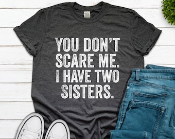 May include: A dark gray t-shirt with the text "You don't scare me. I have two sisters." printed in white.
