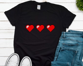 May include: Black t-shirt with three red pixelated hearts in a row. The hearts are in the style of a video game health bar.