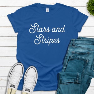 Könnte beinhalten: Ein königsblaues T-Shirt mit dem Text "Stars and Stripes" in weißer Kursivschrift.