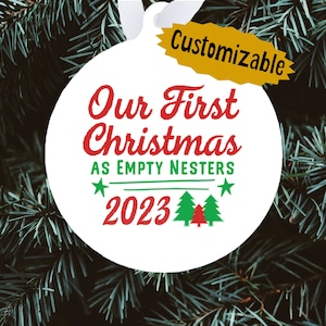 May include: White round Christmas ornament with red and green text that reads "Our First Christmas as Empty Nesters 2023" with a green Christmas tree graphic. The ornament has a gold tag that reads "Customizable".