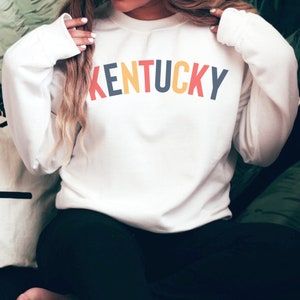 May include: White sweatshirt with the word "KENTUCKY" written in a rainbow arch across the front.